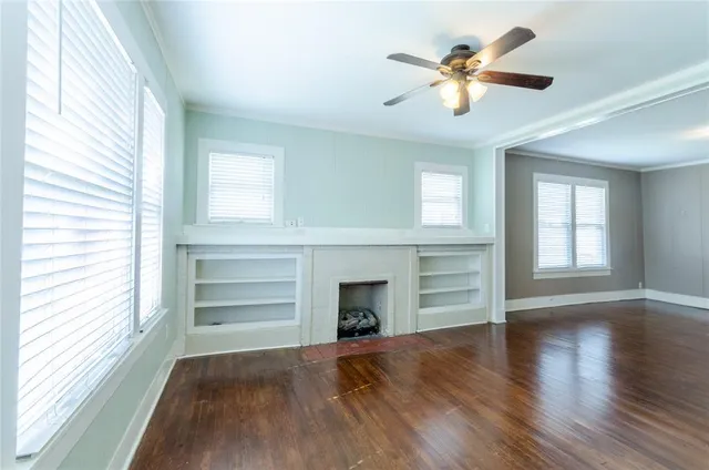 an empty room with wooden floor ceiling fan and windows