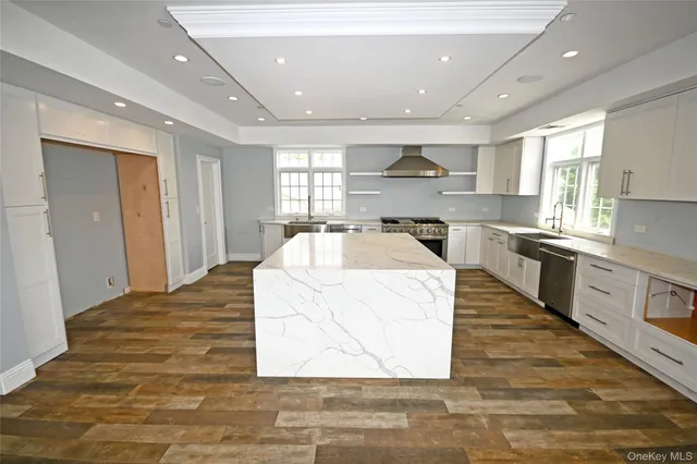a large white kitchen with kitchen island a stove a sink a refrigerator and white cabinets with wooden floor