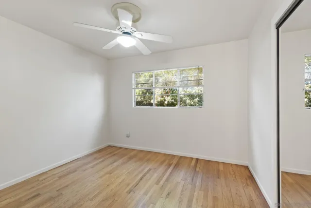 an empty room with wooden floor chandelier fan and windows