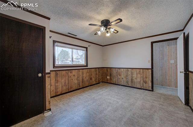 6773 Dale Road Colorado Springs, CO 80915 - Photo 34 of 45 Unfurnished bedroom featuring a wainscoted wall, visible vents, ornamental molding, and a textured ceiling