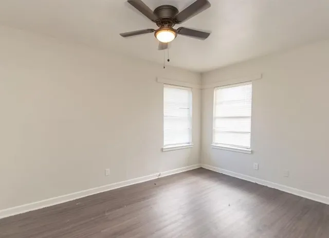 an empty room with wooden floor ceiling fan and window