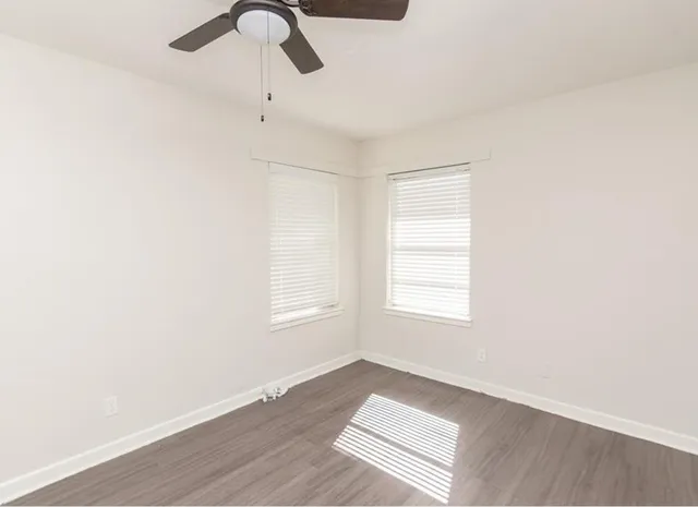 a view of an empty room with chandelier fan and wooden floor