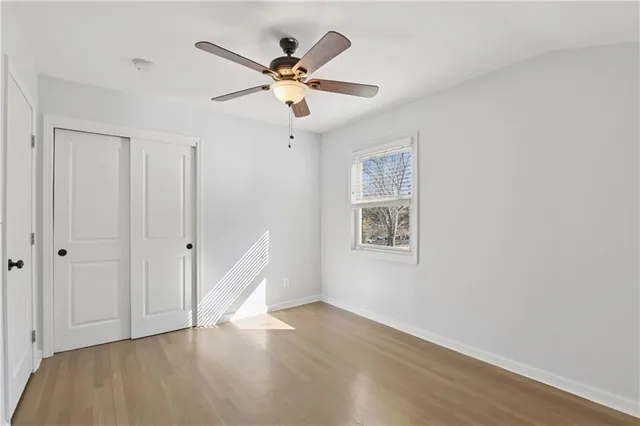 a view of an empty room with wooden floor and a ceiling fan