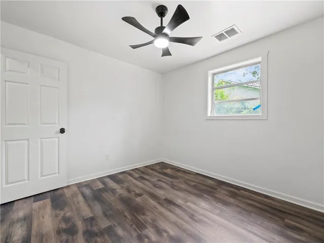 an empty room with wooden floor ceiling fan and window