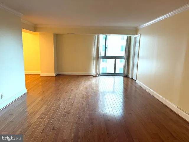 a view of an empty room with wooden floor and a window
