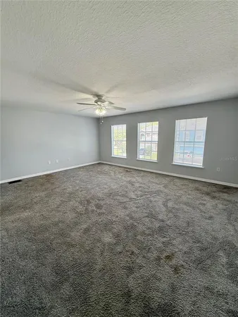 an empty room with a chandelier fan and windows
