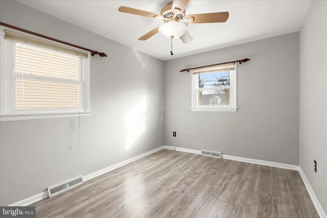 an empty room with wooden floor chandelier fan and windows