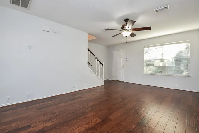 an empty room with wooden floor ceiling fan and windows