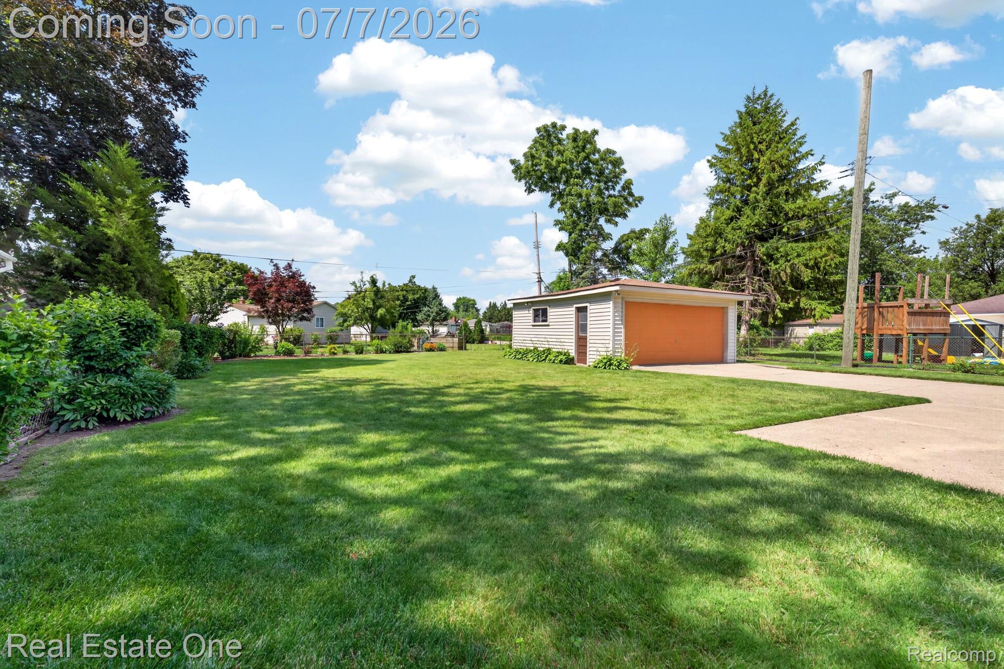 24749 Munson Street Taylor, MI 48180 - Photo 26 of 28 Expansive backyard featuring a manicured lawn, established landscaping, detached garage with orange door, and a concrete driveway