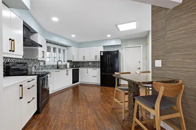 a kitchen with stainless steel appliances kitchen island granite countertop a refrigerator a stove a sink dishwasher and white cabinets with wooden floor