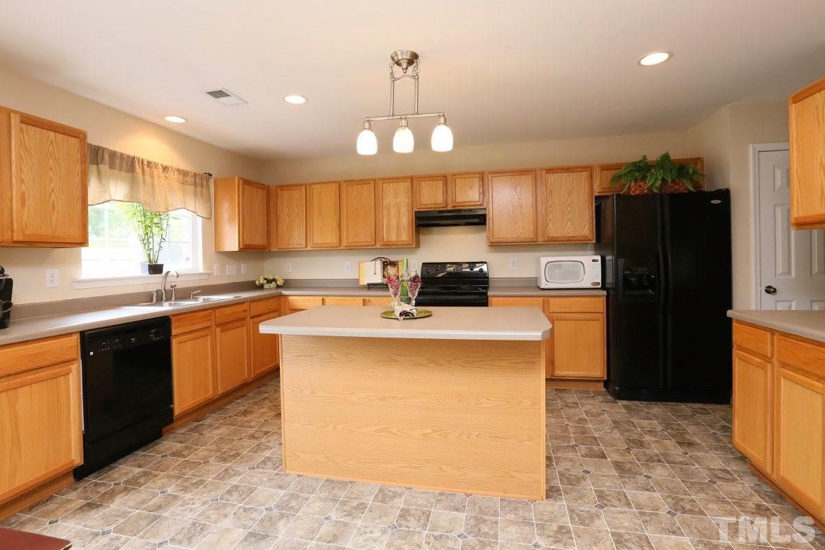 5944 Ricker Road Raleigh, NC 27610 - Photo 11 of 25 a kitchen with granite countertop a refrigerator a stove top oven a sink and cabinets