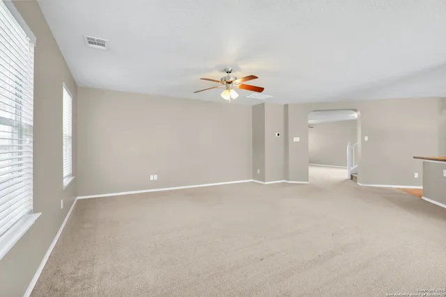 an empty room with windows and chandelier fan