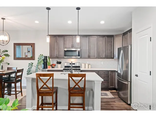 a kitchen with stainless steel appliances granite countertop a stove top oven a refrigerator a sink a dining table and chairs with wooden floor