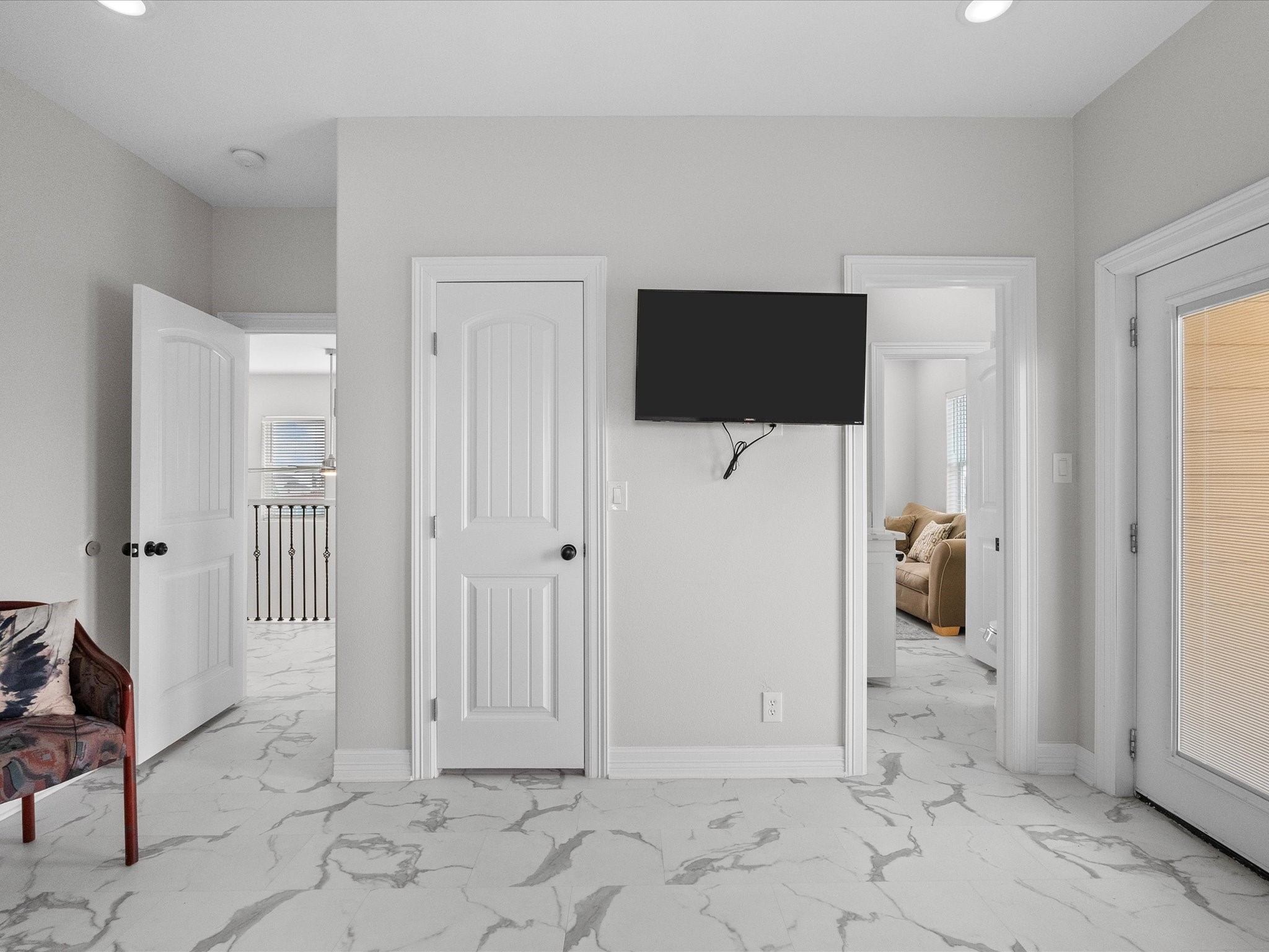 1018 Seashell Drive Surfside Beach, TX 77541 - Photo 39 of 49 This photo showcases a bright, modern room with marble-style flooring. It features multiple doors leading to other areas, a wall-mounted TV, and ample natural light from a glass door. The neutral tones create a versatile space.