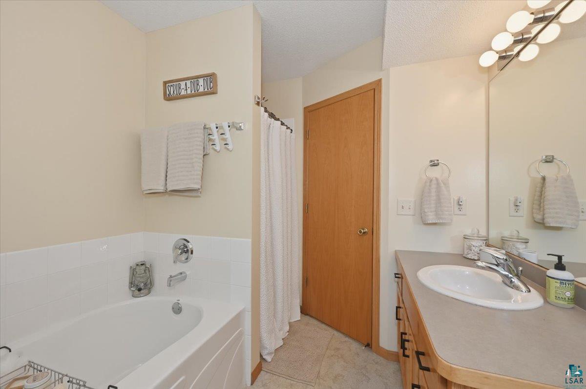 47 Amy Lane Esko, MN 55733 - Photo 13 of 33 Bathroom featuring a built-in tub with white subway tile surround, a single vanity with an integrated sink, a large mirror, and an overhead vanity light fixture