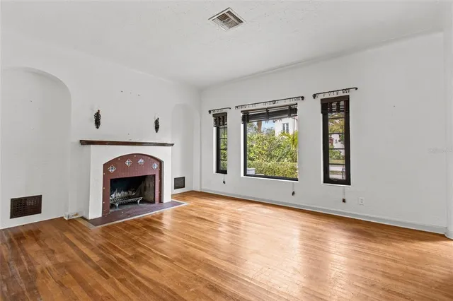 a view of an empty room with wooden floor fireplace and a window