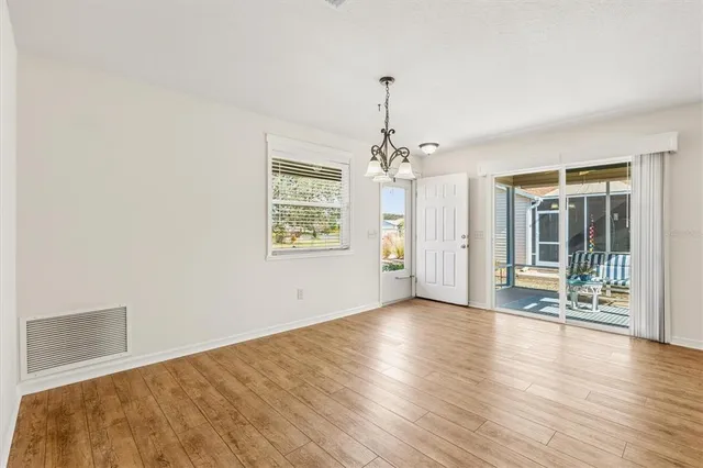 an empty room with wooden floor chandelier and windows