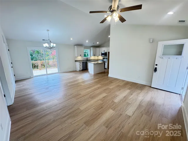 a view of an empty room with wooden floor ceiling fan and kitchen view
