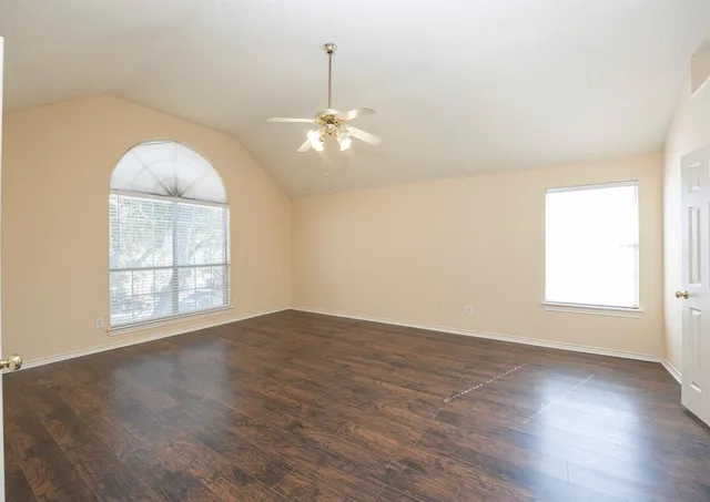 an empty room with wooden floor chandelier fan and windows
