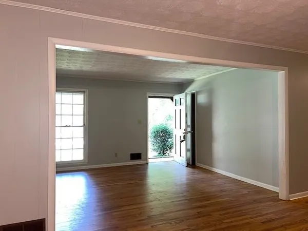 an empty room with wooden floor and windows with curtains
