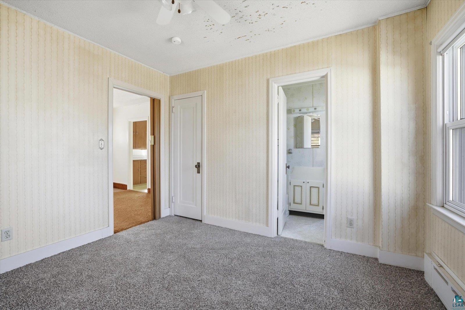 709 Michigan Street Hibbing, MN 55746 - Photo 10 of 47 Unfurnished bedroom featuring baseboard heating, light carpet, connected bathroom, a textured ceiling, and wallpapered walls