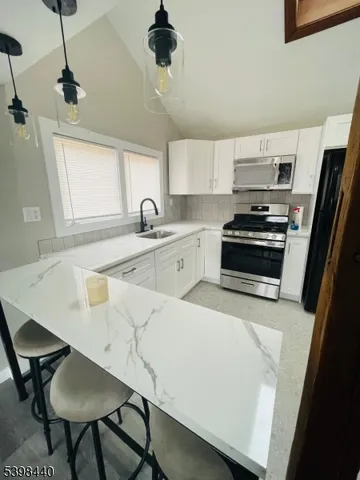 a kitchen with stainless steel appliances a stove a sink a microwave a dining table and chairs with wooden floor