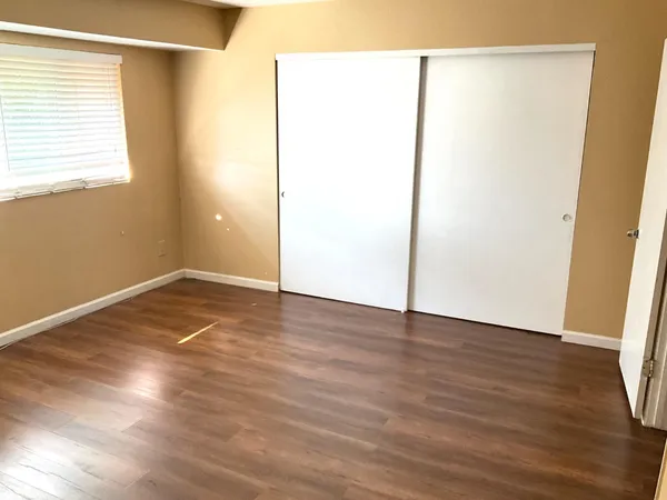 a view of an empty room with wooden floor and a window