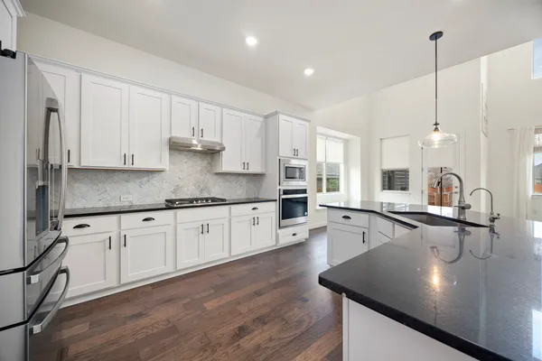 a kitchen with stainless steel appliances granite countertop a sink a stove and white cabinets with wooden floor
