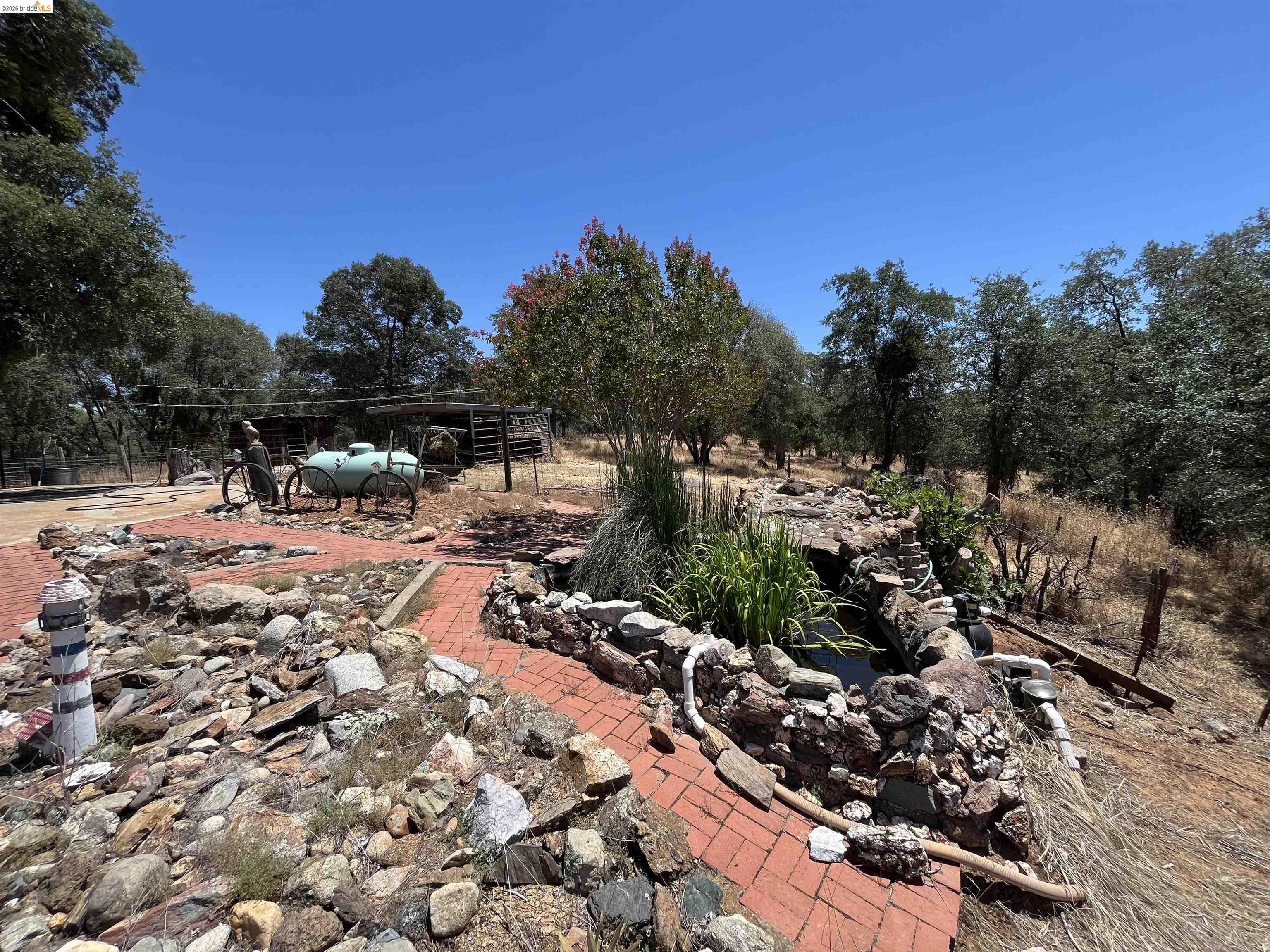 18195 Wards Ferry Road Sonora, CA 95370 - Photo 43 of 67 Outdoor area featuring a stone-lined water feature, brick pathways, mature trees, and natural landscaping