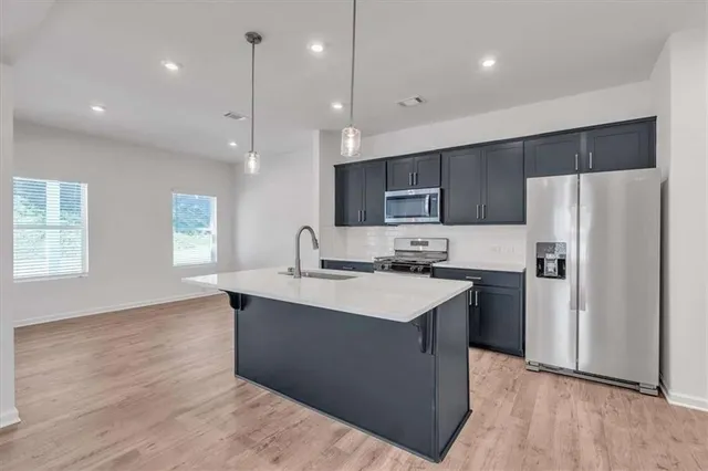 a kitchen with stainless steel appliances granite countertop a sink a stove a refrigerator and island with wooden floor