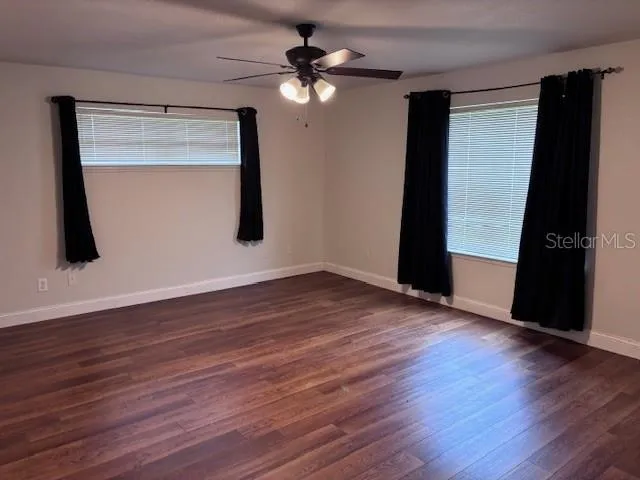 a view of an empty room with wooden floor and a ceiling fan
