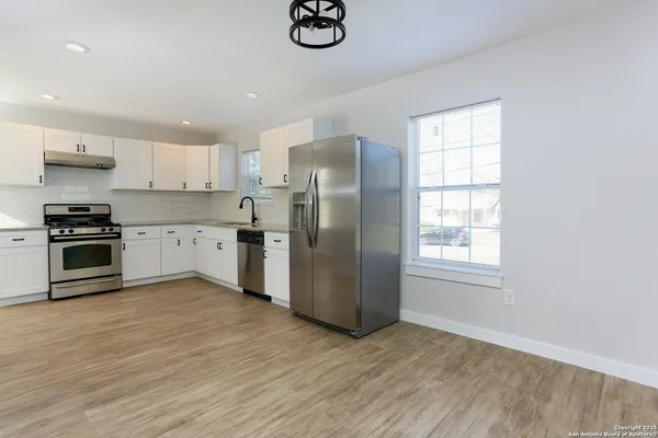 a kitchen with stainless steel appliances granite countertop a refrigerator a sink dishwasher a stove with white cabinets and wooden floor