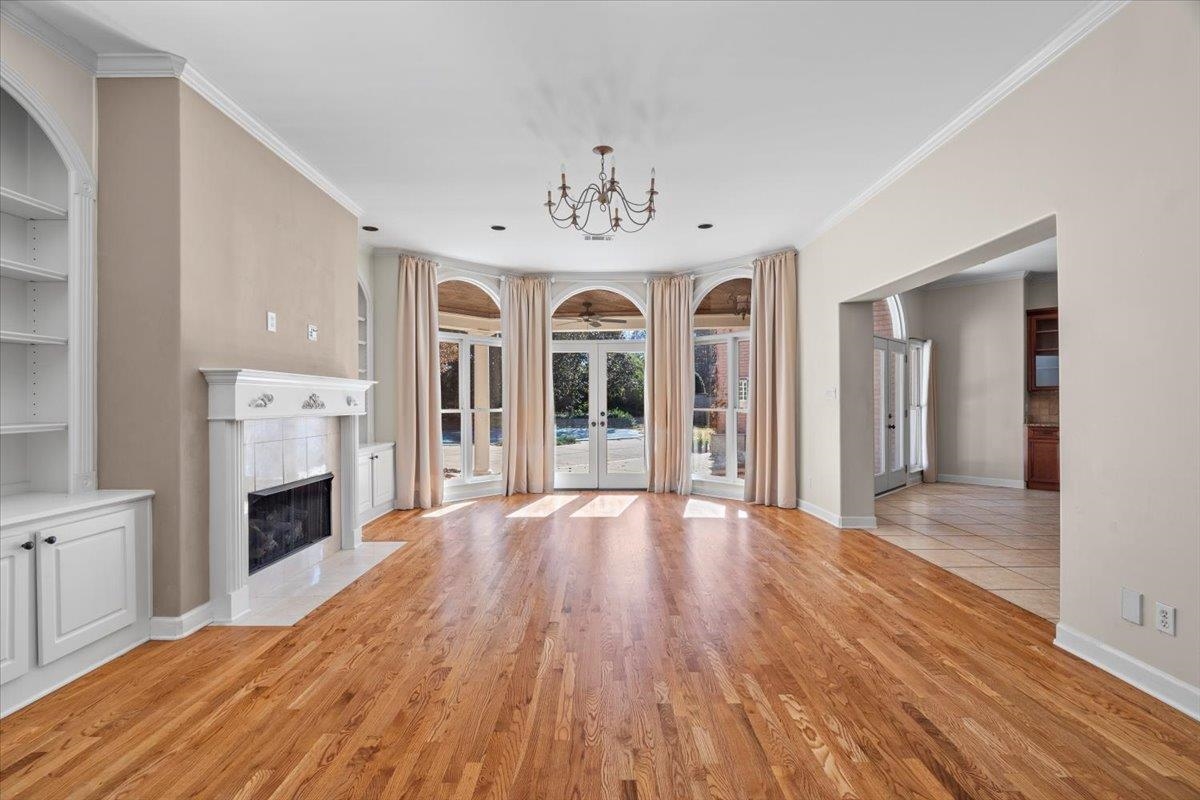 170 Jamerson Farm Road Collierville, TN 38017 - Photo 9 of 40 Unfurnished living room featuring crown molding, a tile fireplace, built in features, an inviting chandelier, and light hardwood / wood-style flooring
