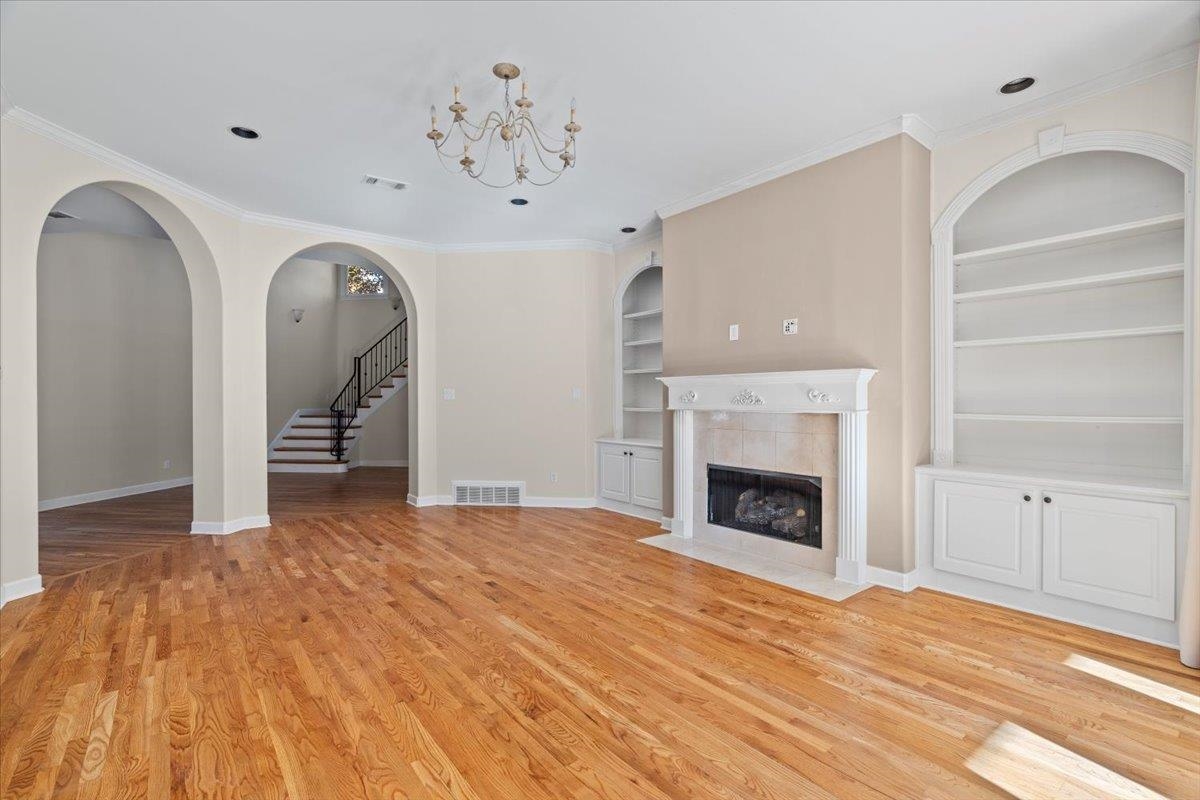 170 Jamerson Farm Road Collierville, TN 38017 - Photo 10 of 40 Unfurnished living room featuring built in shelves, a tile fireplace, a notable chandelier, crown molding, and wood-type flooring
