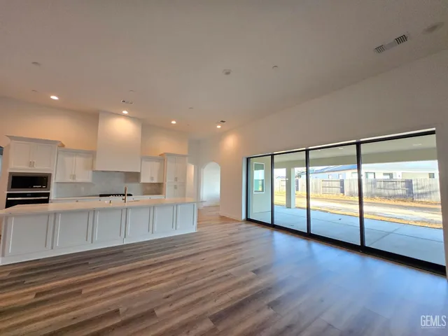 a view of an empty room with kitchen and wooden floor
