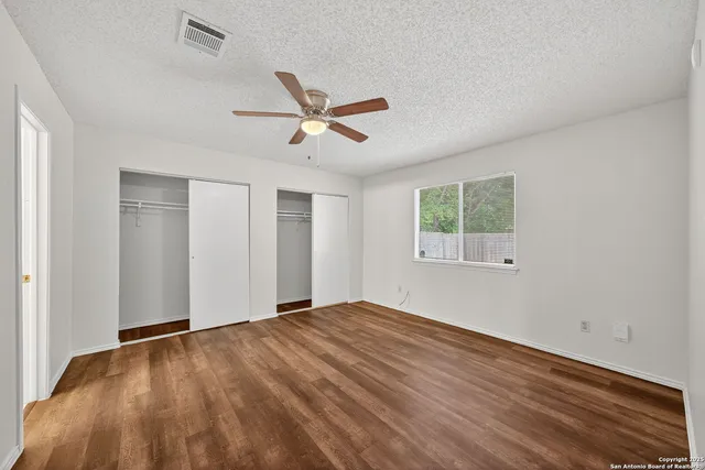 a view of empty room with wooden floor and fan