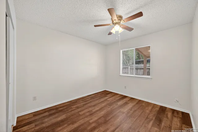 a view of an empty room with wooden floor and a ceiling fan