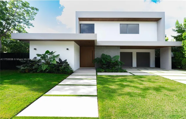 a view of a house with a yard plants and large tree