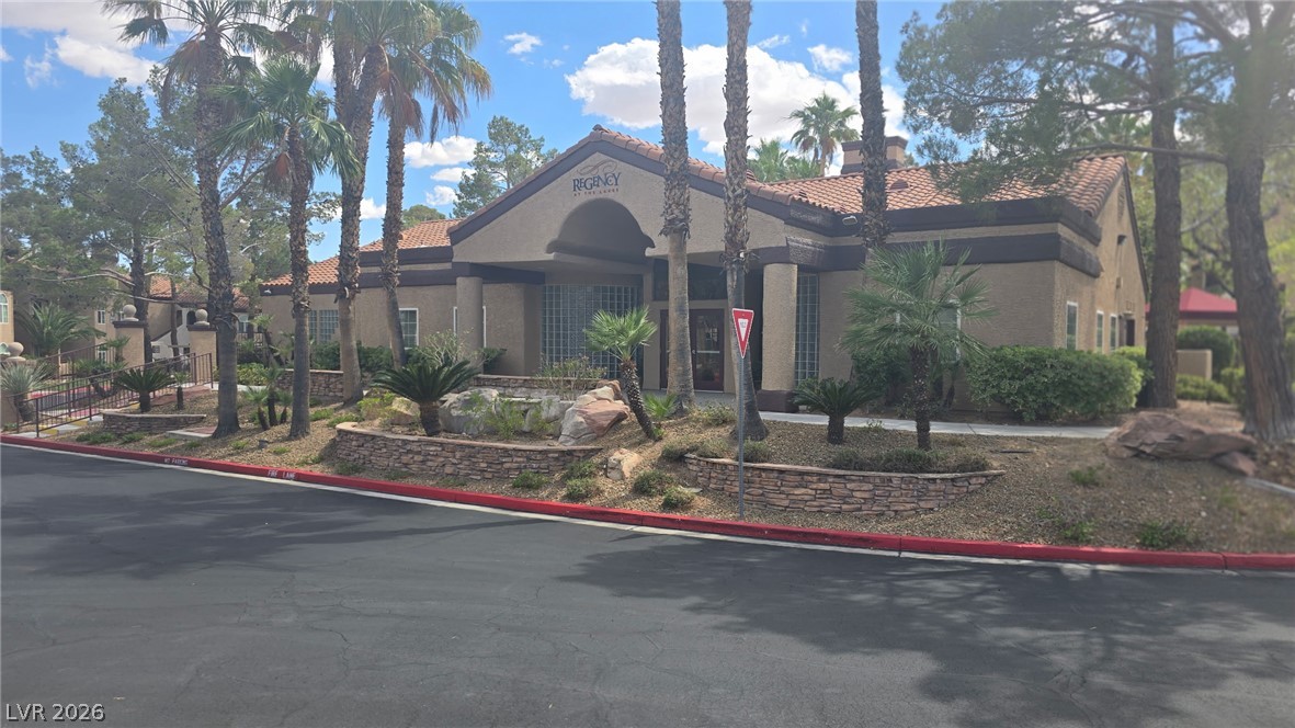 9325 West Desert Inn Road, Unit 123 Las Vegas, NV 89117 - Photo 33 of 36 A terracotta-roofed clubhouse offers a welcoming entrance with lush landscaping and mature palm trees.