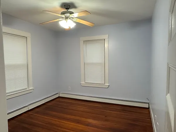 an empty room with wooden floor chandelier fan and windows