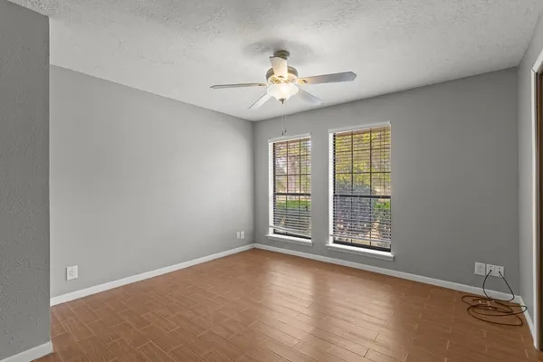 an empty room with wooden floor fan and windows