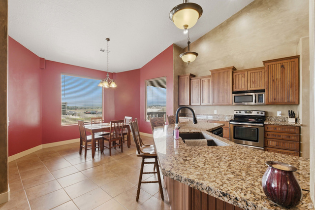 2567 West Rim Rock Drive Stockton, UT 84071 - Photo 13 of 64 Kitchen featuring a granite-topped island with an undermount sink, wood cabinetry, stainless steel appliances, and tile flooring