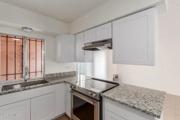 a kitchen with granite countertop a sink stainless steel appliances white cabinets and a window