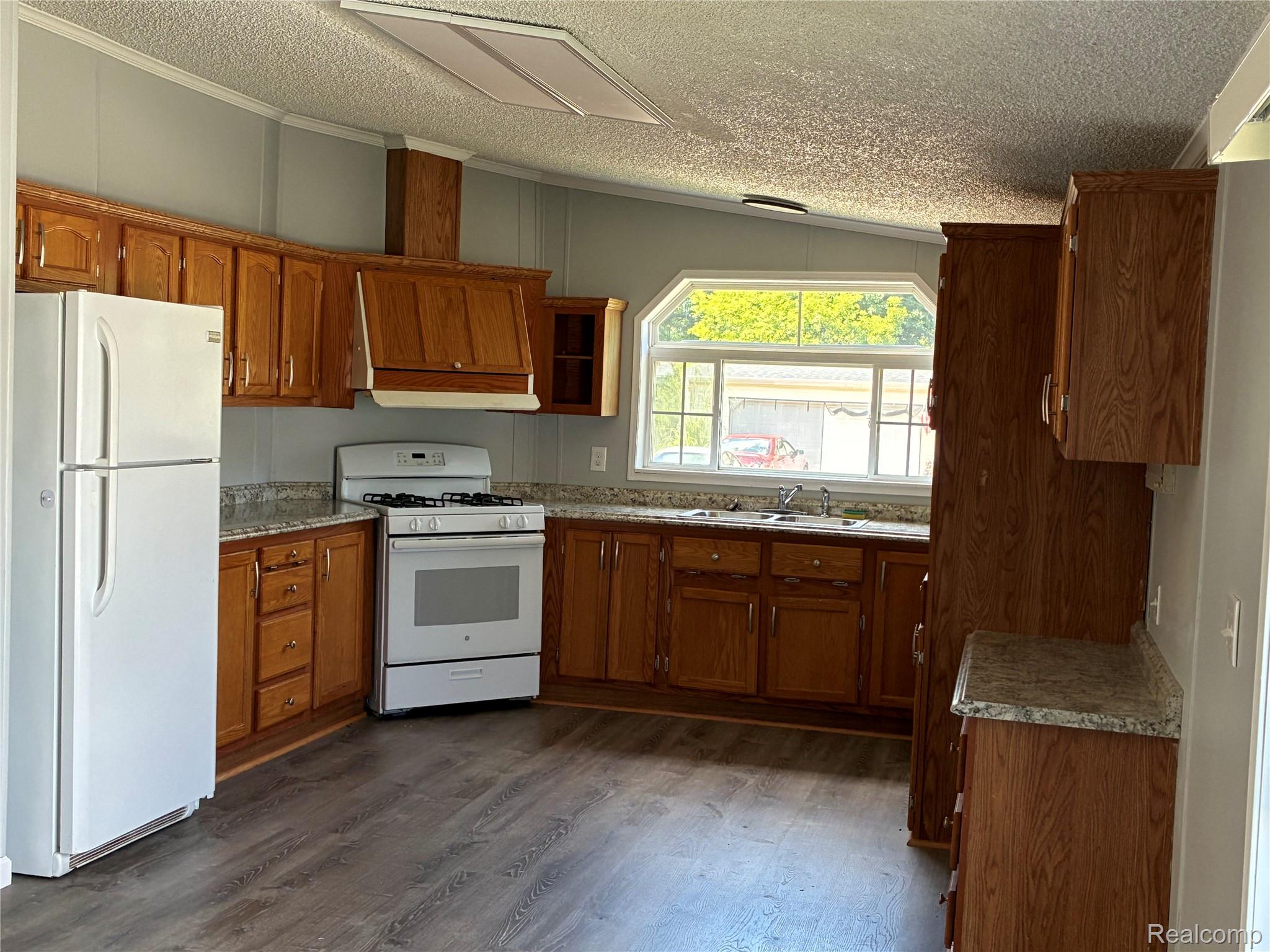 420 Hidden Ridge Road Morrice, MI 48857 - Photo 6 of 16 Kitchen featuring white appliances, wood finish cabinets, a textured ceiling, dark wood finished floors, and ornamental molding