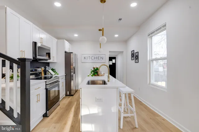 a kitchen with stainless steel appliances kitchen island granite countertop a stove a sink a refrigerator white cabinets and wooden floor