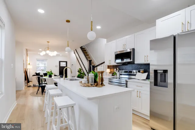a kitchen with stainless steel appliances kitchen island granite countertop a refrigerator a stove a sink a dining table and chairs with wooden floor