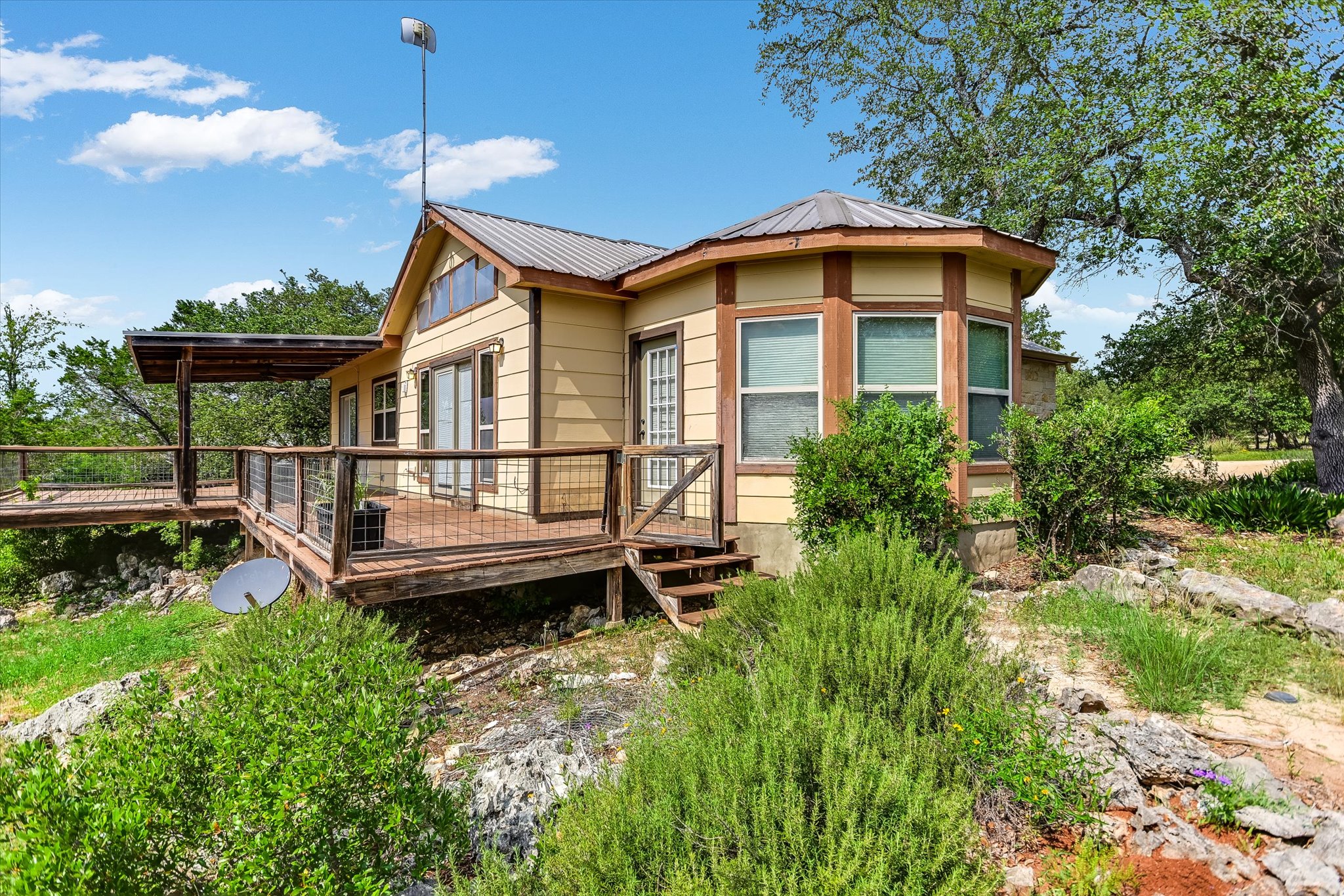700 Cliffside Road Wimberley, TX 78676 - Photo 15 of 22 Yellow siding with brown trim, featuring a metal roof and an extensive wood deck