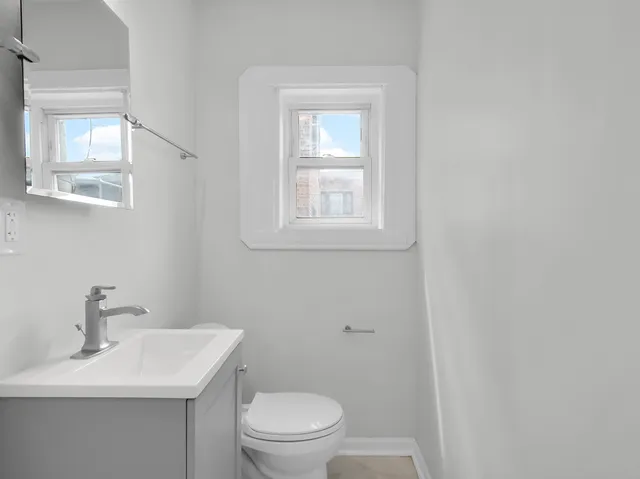 a bathroom with a toilet a sink a mirror and a window