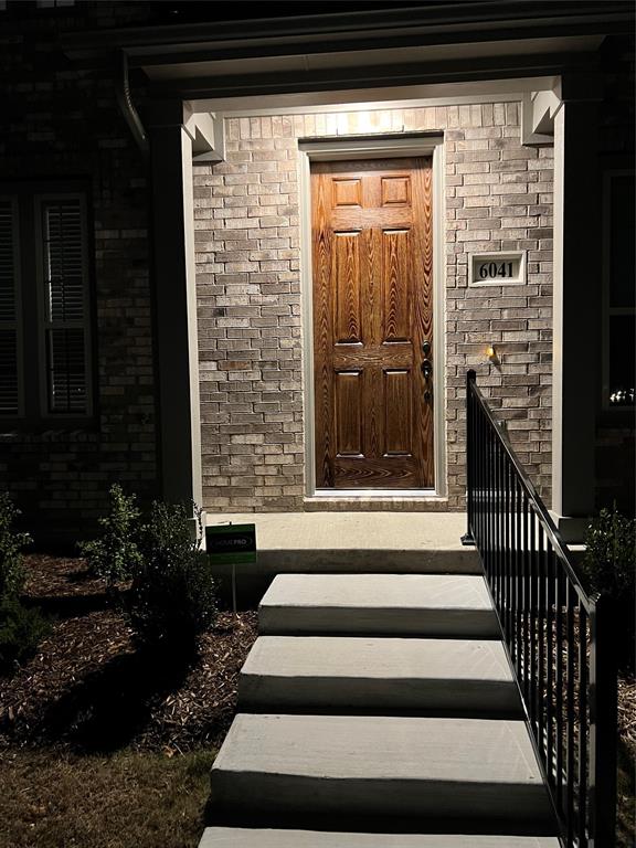 6041 Roper Road McKinney, TX 75070 - Photo 2 of 24 Entryway featuring a paneled wood-finish door, brick facade, concrete steps, wrought iron railing, and manicured landscaping