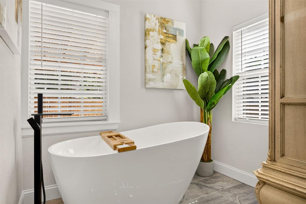 702 West Spring Street Weatherford, TX 76086 - Photo 14 of 39 Freestanding soaking tub with a matte black floor-mounted faucet, set against a backdrop of light gray walls and large-format gray floor tiles
